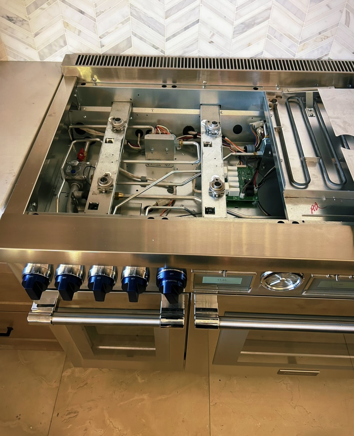 Professional stainless gas range with the top removed, exposing burners and control board during repair