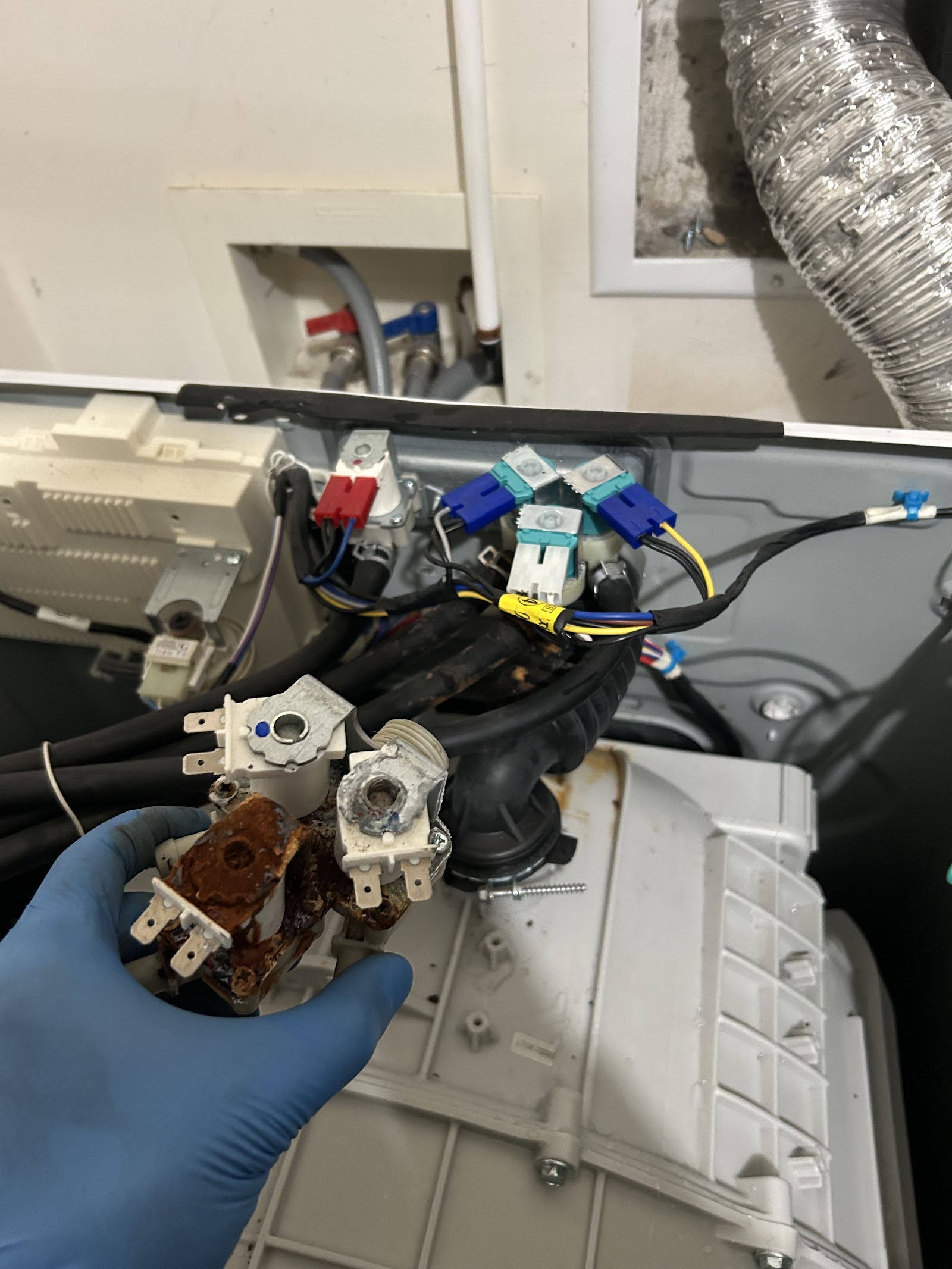 Gloved hand holding a heavily rusted water inlet valve removed from a washer