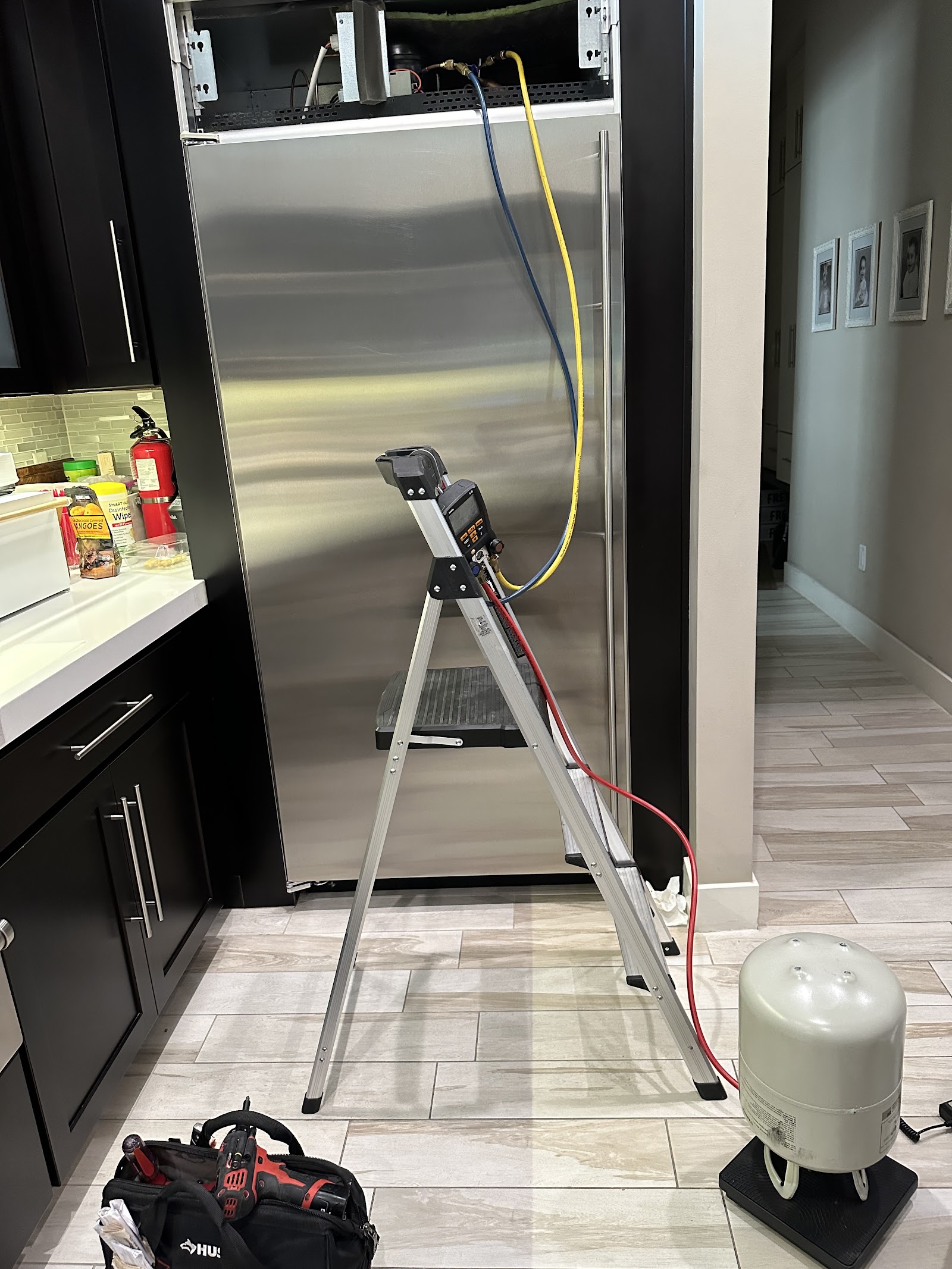 Built-in stainless refrigerator being serviced with refrigerant gauges and a recovery tank